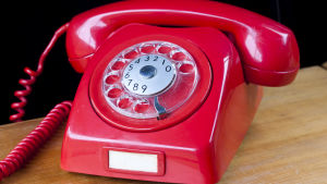 En märklig kvarleva. Kunde man ens ringa med den? Röd trådtelefon från sjuttiotalet på ljusbrunt träbord.