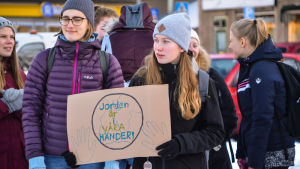 Elever på klimatstrejk i januari i Borgå. Ungdomar protesterar mot klimatförändringen. I förgrunden synns två unga kvinnor varav den ena håller upp en skylt på vilken det står "Jorden är i våra händer!".