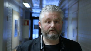 Christian Lindedahl. En medelålders man med grått kort hår och skägg står i en korridor.