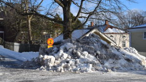 Snömängderna samlas på olika håll. En stor snöhög täcker nästan trafikmärket.