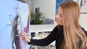 Riitta Kuisma studerade konst i Moskva och flyttade sedan till Hongkong. Där har hon livnärt sig som konstnär i 20 år. Riitta Kuisma målar i Hongkong. På bilden syns hon med en pensel i handen och målar en tavla