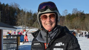 Sari Fahlbom ler ikapp med solen. Skidläraren Sari Fahlbom, en dam med svart jacka, grå hjälm, solglasögon och skidglasögon.
