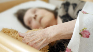 En äldre kvinna ligger i en sjukhussäng. 