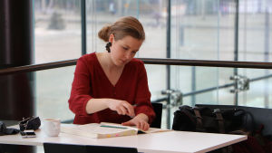 Dirigentstuderande Emilia Hoving fick hoppa in plötsligt för att dirigera Radions symfoniorkester. Emila Hoving sitter vid ett bord och studerar ett orkesterpartitur, med stora glasfönster i bakgrunden.