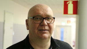 Kari Häggblom (SDP). En medelålders flintskallig man med glasögon står i en vit korridor.