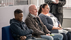 Kino: Minä, Daniel Blake. Poika, mies ja nainen istuvat jonkinlaisella odotuspenkillä.