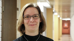 Mikaela Björklund, ordförande för stadsfullmäktige i Närpes. En kvinna med glasögon och axellångt brunt hår står i en korridor.