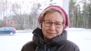 Marianne Nygård. En kvinna i 60-årsåldern med en rosa mössa på huvudet står på en parkeringsplats.