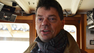 Ted Lönnroos. En medelålders man står inne i en kajuta. Närbild på hans ansikte. Han tittar in i kameran med ett litet leende.