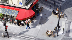Gatucaféerna i Paris har kvar sin charm, men vardagens realism lurar bakom hörnet. En bild tagen från ovan av ett café i ett gathörn i Paris
