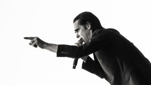 Allt startade med kärleken till Nick Caves musik. Svartvit bild på Nick Cave i mörk kostym live mot en vit himmel. Cave i profil pekar med fingret framåt.