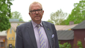 Stadsdirektör Ragnar Lundqvist lobbar i kulisserna. Man med glasögon iklädd skjorta, slips och kavaj ser mot kameran. Vädret är mulet och i bakgrunden finns träd och hus.