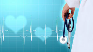 En hand håller i ett stetoskop mot en blå bakgrund med ljusa hjärtan och en hjärtfilm.
