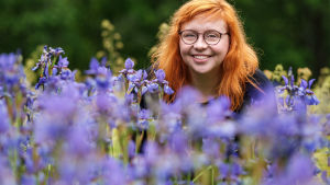 Annika Ljungberg är mångsysslare inom biologin. Naturväktarnas programledare Annika Ljungberg kikar fram bakom blåa blommor.