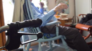 Kvaliteten på palliativ vård och hospice bör stärkas över hela landet konstaterar man i THL:s färska rapport. handtaget av en rollator i förgrunden. Harry i sin gungstol i bakgrunden