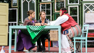 Systrarna Gunilla (Patricia Hirn), Carina (Petra Sundqvist) och Eivor (Katarina Nikkanen). Tre kvinnor sitter runt ett bord och håller varandra i händerna.