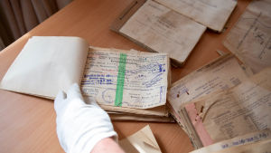Dokument från 1944 då tyska soldater fanns i Hangö som hittades 2019 i en ventilationskanal i Hangö hamn. På bilden syns en hand bläddra genom ett häfte med text skriven på tyska och med många stämplar.