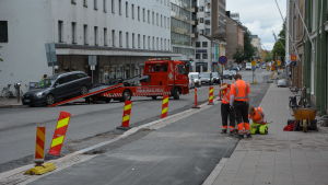 I dag ska det asfalteras, och de bilar som står kvar trots flyttningsuppmaningen bogseras bort. Tre personer arbetar på en trottoar. Bredvid dem bogseras en bild bort.