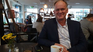 Owe Sjölund vill se en stadsdirektör som tar tag i projekt och frön av möjligheter. Owe Sjölund sitter på ett kafé med en kopp kaffe.