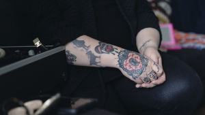 Anna Giss pitää tatuoituja käsivarsiaan sylissään. Hänen vierellään kuvan vasermmassa laidassa on meikkipakki.
