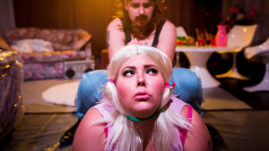 Josefine Fri och Emelie Zilliacus från Glitcher iscensatte porrfilmskonventioner i föreställningen The Porn Horror Musical hösten 2019. Glitcher återkommer nu med kortfilmen Distant Dildos. Skådespelaren Josefine Fri i förgrunden med en blond peruk på huvudet. Bakom henne Emelie Zilliacus.
