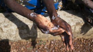 Barn tvättar händerna utanför en skola i byn Sintchan-Farba i Guinea-Bissau i januari 2020. Nu har alla skolor stängts också i Guinea-Bissau. Foto: Unicef/Prinsloo. Två händer som tvättas under rinnande vatten.
