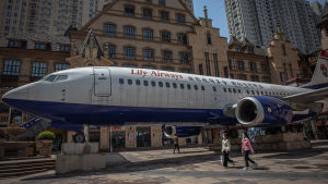 Coronapandemin fick sin början i miljonstaden Wuhan människor i ansiktsmask promenerar förbi ett flygplan som ställts ut i ett shoppingdistrikt i Wuhan