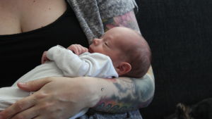 Ett litet spädbarn som ligger i famnen på en kvinna med tatuerad arm.