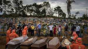 Flera kistor på rad på en begravningsplats i Manaus i Brasilien. Bredvid kistorna står skyddsklädda människor