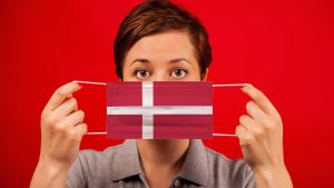 Munskydd är inte så populära i Danmark Kvinna framför röd bakgrund med munskydd, i danska flaggans färger.