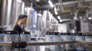 Ett ölbryggeri där ölburkar färdas på en produktionslinje. En kvinna övervakar produktionen.