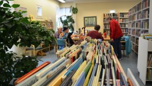 Tessjö bibliotek, där också postkontoret finns, får fortsätta sin verksamhet. Arkivbild. Bild inifrån ett bibliotek. I förgrunden syns böcker, i bakgrunden äldre damer kring ett bord.