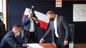 Sittande presidenten Andrzej Duda röstade i Krakow under söndagen. En man ger en valsedel till en annan man, båda bär munskydd. En tredje man fotograferar.