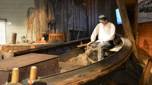 En docka som föreställer en fiskare sitter i en gammal träbåt.