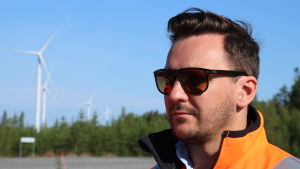 Enligt Michael Sandberg på Prokon ger det goda samarbetet med Neoen en trygghet för framtiden. En man med solglasögon och kort mörkt hår står vid en skogsöppning. I bakgrunden syns fyra vindmöllor.
