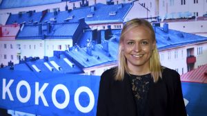 Elina Lepomäki på partikongressen i Björneborg. Hon är en av Samlingspartiets tre viceordförande. porträttbild av Elina Lepomäki framför storbild med hustak och en del av Samlingspartiets logo