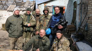 “Utrikesjournalistik skulle inte vara möjligt utan lokala medarbetare”. Här är Antti Kuronen på uppdrag i Ukraina. Antti Kuronen poserar med lokala män i kamouflagekläder i Ukraina med tv-kamera i handen.