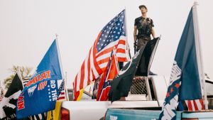 En parad med Trumpanhängare och QAnon-flaggor. Konspirationsteorierna har ökat under coronapandemin. En man omgiven av flaggor står på flaket till en pick-up