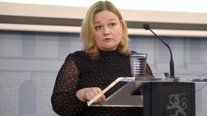 Minister Krista Kiuru. Krista Kiuru står bakom ett podium med en mikrofon framför sig.