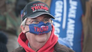 Munskydd som coronaskydd har inte varit en naturlig sak för Trump och hans anhängare. Manlig Trump-anhängare med coronaskydd över näsan.