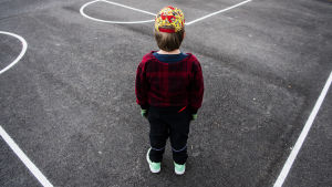 En pojke står på en asfalterad plan med ryggen mot kameran.