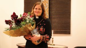 Mari Leppänen hoppas att hon ska kunna inspirera andra kvinnor att våga hitta sin egen plats inom kyrkan. En kvinnlig präst står med en blombukett och en bok i famnen.