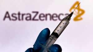 Astrazenecas vaccin är betydligt billigare än de från Pfizer och Moderna. En hand håller i en spruta. I bakgrunden texten AstraZeneca.