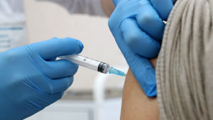Ett par händer instuckna i blå plasthandskar vaccinerar en person. 