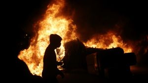Tiotals demonstranter och poliser har skadats under kravallerna Siluetten av en demonstrant syns framför en brinnande barrikad