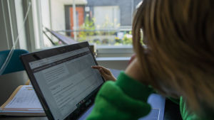 Undervisningen har blivit mer digitaliserad till följd av coronaepidemin. Skolelev i grön huvtröja sitter vid en dator.