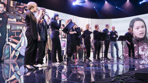 Årets festkonsert har spelats in sektionsvis i Schaumansalen i Jakobstad. En proffsig kör uppträder på scenen i Schaumansalen i Jakobstad.