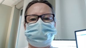 Petra Ingvesback tackar munskyddet för att hon klarade sig osmittad på jobbet. En kvinna med glasögon, läkarrock och munskydd tar en selfie.