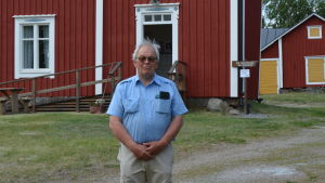 Håkan Nylund framför Strömmersgården som är inredd i tidstypisk stil. Håkan Nylund står framför ett rött hus.