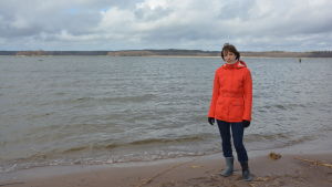 Anna-Karin Almén har alltid velat forska i plankton eftersom det är fascinerande att se vad som finns i en droppe vatten. Hon gick med i ett stort projekt där man skulle simulera havsförsurningen utanför Tvärminne och började då forska i hoppkräftor. En kvinna i orange jacka och blå byxor står på en strand med vågor som rullar in. Hon heter Anna-Karin Almén.